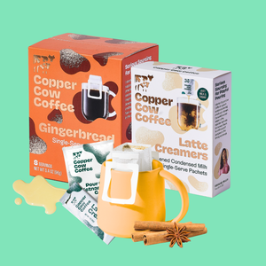 Copper Cow Coffee gingerbread single-serve packets shown with their orange and white packaging boxes, alongside a yellow mug filled with packets, cinnamon sticks, and a star anise on a solid mint green background.