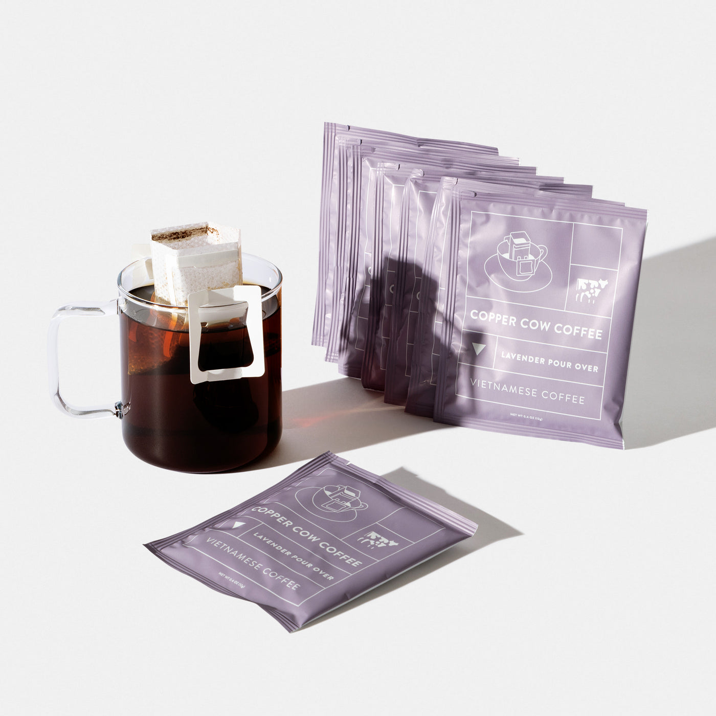 8-pack: 8-Pack of Lavender Vietnamese Coffee single-serve pour over pouches next to black cup of brewing coffee.